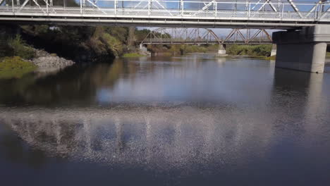 Drohne-Fliegt-Rückwärts-Unter-Der-Neuen-Fachwerkbrücke-Mit-Der-Alten-Brücke-Im-Hintergrund-Am-Russian-River-In-Healdsburg,-Kalifornien