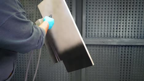 Man-applying-black-anti-corrosion-powder-coating-to-metal-sheet-using-a-spray-gun-in-factory