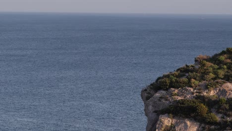 Luftaufnahme-Des-Randes-Einer-Klippe-Mit-Dem-Meer-Im-Hintergrund-Auf-Der-Insel-Sardinien-Im-Mittelmeer-Von-Italien-Bei-Sonnenuntergang,-Mittlere-Aufnahme