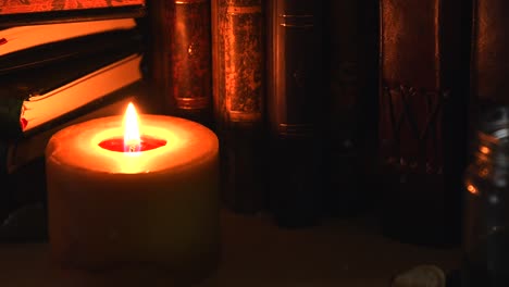 Close-up-background-of-an-ancient-library,-next-to-a-frieplace,-with-old-books,-ink-and-a-candle-with-flickering-flame,-with-some-dust-flying-around