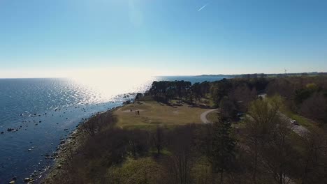Aerial-Shot-of-The-Forest-Near-Ystad-Saltsjöbad-in-South-Sweden-With-A-Car-Passing-By-and-a-Few-People-Gathering-by-The-Grass