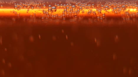 Abstract-veiw-Macro-close-up-of-a-glass-of-beer-beverage-with-active-fizzy-bubbles-of-Co2-gas,-carbon-dioxide-orange-gold-background