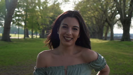 Slow-Motion-Portrait-of-a-gorgeous-hispanic-latino-young-woman-looking-at-the-camera-and-show-emotions-from-serious-to-smiling-and-laughing-with-a-beautiful-British-park-in-the-background