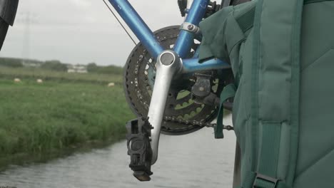 Close-up-shot-of-an-empty-bicycle-pedal-and-backpack-with-a-river-stream-in-the-background