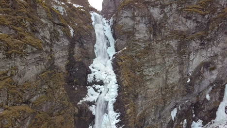 Aerial-View-of-an-Icy-Waterfall-Cutting-Through-a-Cliff-in-Norway,-Slow-Decending-Motion