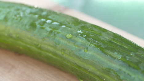 Close-up-pan-of-a-freshly-rinsed,-whole-cucumber-resting-on-a-wood-cutting-board