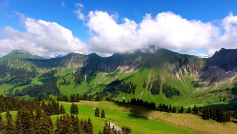 Aerial-shot-over-Alpine-landscape,-Switzerland-in-spring-Forest-and-Alpages,-summits-in-the-background-in-the-clouds