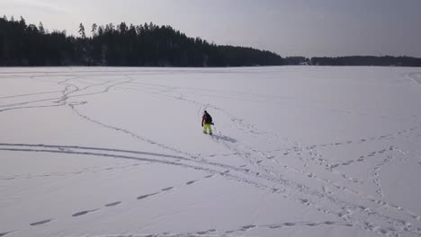 Wide-aerial-view-of-lone-fisherman-walking-over-frozen-lake-searching-for-the-ideal-spot-to-sink-a-hole