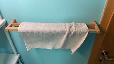 Unique-way-of-putting-new-fresh-towel-on-wooden-holder-in-bathroom-with-green-blue-wall