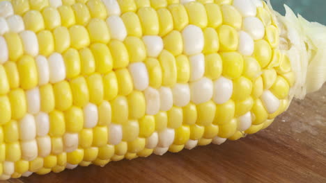 Slow-motion-close-up-of-a-fresh,-ripe-corn-on-the-cob-rolling-along-a-wood-cutting-board