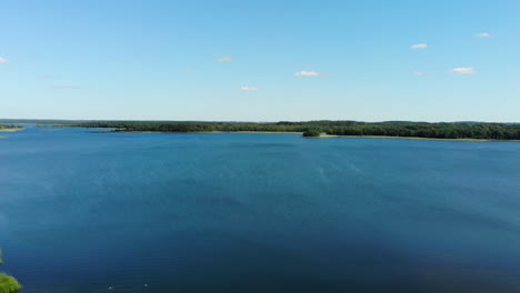 AERIAL:-Drone-Lift-Up-Above-Beautiful-Blue-Lake-With-Forest-Line-Visible-in-the-Horizon