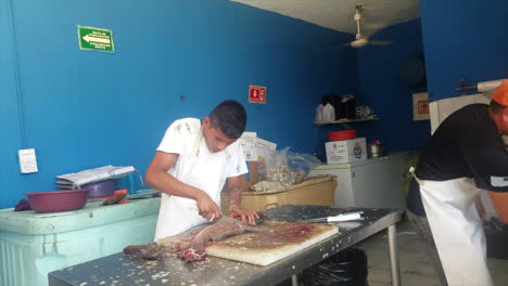 Chef-In-A-Restaurant-In-Mexico-Cuts-Up-A-Fish-With-A-Knife-And-Meat-Cleaver-Into-Pieces-On-A-Cutting-Board-In-The-Kitchen