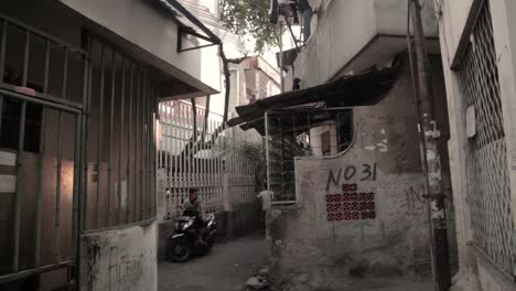 South-east-asian-with-motorbike-driving-in-an-alley-and-a-person-sitting-on-a-motorbike,-somewhere-in-Jakarta