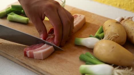 Close-up-of-Male-hand-cutting-pork-belly-on-wooden-cutting-board-into-strips
