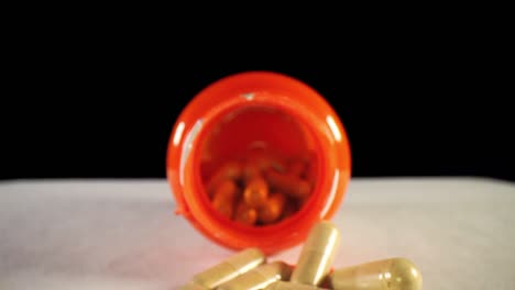 moving-past-capsules-in-cap,-pushing-towards-the-opening-of-an-orange-supplement-pill-bottle