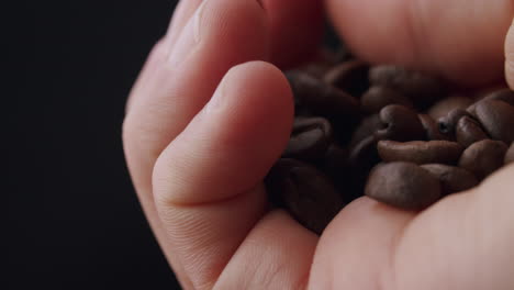 Kaukasische-Hand-Hält-Ein-Bündel-Gerösteter-Kaffeebohnen-Und-Inspiziert-Die-Bohnen-Mit-Dem-Daumen