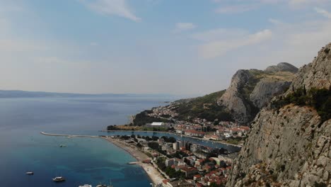 Hazy-sunny-summer-day-aerial-approach-footage-over-Omis-town,-river-Cetina-and-cliffs