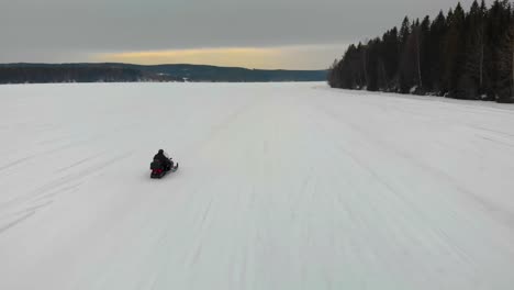 Tracking-aerial-shot-of-a-man-driving-his-snowmobile-on-Indalsalven-in-Timra,-Sundsvall,-Sweden