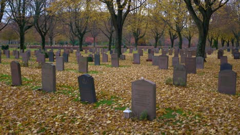 A-graveyard-covered-in-leaves-on-an-autumn-day-in-Kviberg-cemetery-in-Gothenburg,-Sweden---Slow-panning