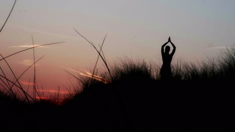 Woman-shilhouette-in-tree-asana-with-raised-arms-over-head-in-dusk