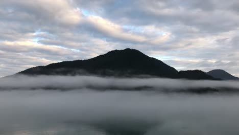 Slow-motion-view-from-a-ship-of-a-dark,-Alaskan-mountain-behind-the-layers-of-the-morning,-ocean-fog