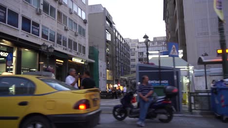 In-car-camera-panning-footage-of-people,-cars-and-stores-in-the-evening-on-a-busy-road-in-Athens