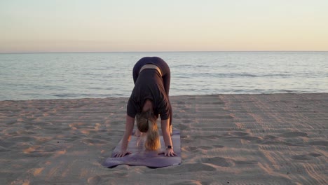 Female-doing-downward-dog-yoga-on-quiet-beach-at-sunset