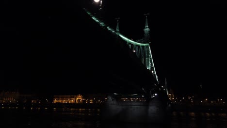 Vorbei-An-Der-Freiheitsbrücke-In-Budapest,-Ungarn,-Mit-Dem-Gellért-Hotel-Und-Dem-Hügel-Mit-Der-Zitadelle-Im-Hintergrund-Auf-Der-Anderen-Seite-Der-Donau-Bei-Nacht