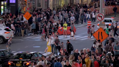 Slow-motion-shot-of-people-crossing-the-street-on-a-crosswalk-and-cars-passing-by-on-a-summer-evening-at-Times-Square-in-Manhattan,-New-York-City,-USA