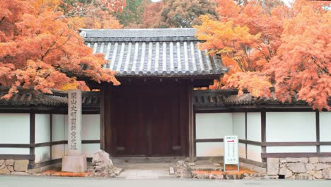 Kleiner-Toreingang-Am-Straßenrand,-Umgeben-Von-Orangefarbenen-Herbstblättern-In-Kyoto,-Japan,-Mittlere-Aufnahme-4k