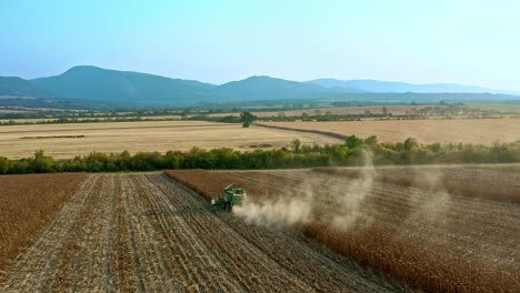 Aerial-view-following-John-Deere-combine-harvesting-sunflower-fields-in-Bulgaria-with-elena-balkans-hills-in-background-and-trailer