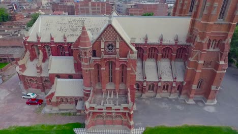 A-beautiful-old-Church-aerial-view,-A-black-kite-sat-at-the-Cross-of-the-Church,-The-Church-with-red-bricks-and-two-cars-parked-at-the-corner