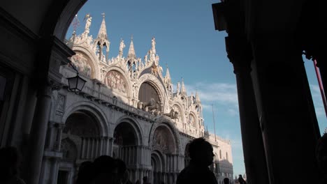 Closeup-of-Saint-Marks-Basilica-with-silhouette-of-tourists-walking-in-Venice,-Italy