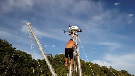 Man-scaling-the-mast-of-Bigkanu-trimaran-sailboat-at-a-coral-reef-spot,-Aerial-pedestal-lift-shot