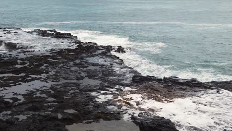 HD-Zeitlupe-Hawaii-Kauai-Von-Rechts-Nach-Links,-Schwenklandung-Mit-Sprudelndem-Hornblasloch-Rechts-Im-Bild-Und-Wasser,-Das-Durch-Ein-Loch-Im-Lavagestein-Links-Im-Bild-Nach-Oben-Wirbelt