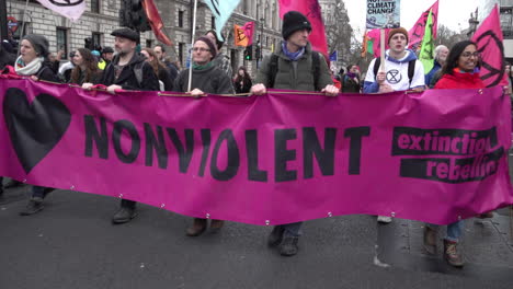 Extinction-Rebellion-climate-change-protestors-march-with-a-large-bright-pink-banner-that-says-“Nonviolent”