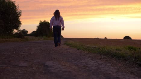 Woman-walking-into-sunset-on-dusty-dry-road-wide-shot