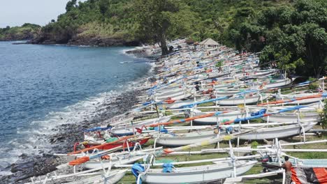 Jukung-fishing-boats-lined-up-on-Amed-beach-as-fishermen-repair-them,-Aerial-flyover-view
