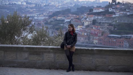 Girl-leaning-on-a-stone-wall-looks-at-camera,-Porto-in-the-background