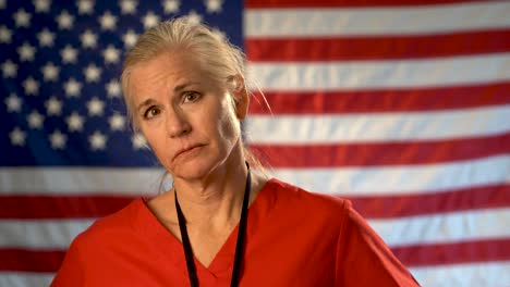 Medium-tight-portrait-of-nurse-looking-extremely-worried-and-sad-with-American-flag-behind-her