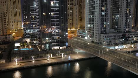 Un-Hermoso-Lapso-De-Tiempo-Del-Puerto-Deportivo-De-Dubai:-Los-Barcos-En-El-Canal-De-Agua,-Una-Carretera-Con-Coches-Que-Crean-Rayas-De-Luz,-Rascacielos-Altos