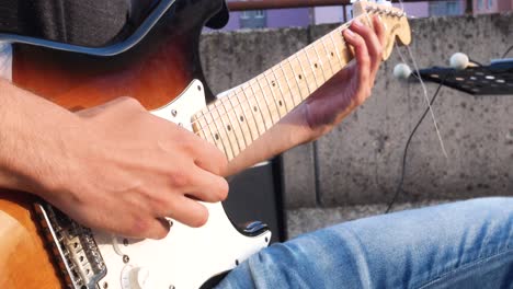 Closeup-of-guitar-player-playing-electric-guitar-on-open-air-concert,-with-visible-colorful-apartment-blocks-in-the-background