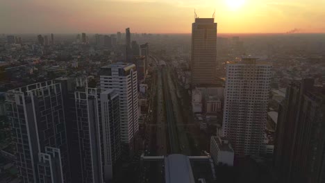 Bangkok-Skyline,-Drone-at-sunset,-BTS-Skytrain-through-the-city