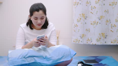 Mujer-Asiática-Feliz-Mirando-Y-Tocando-El-Teléfono-Inteligente-Relájese,-Disfrute-Y-Sonría-Con-Las-Redes-Sociales-En-Línea-En-El-Dormitorio