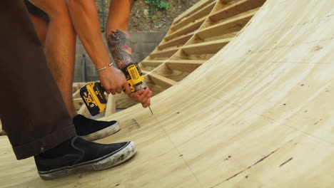 Two-men-use-power-drills-to-secure-a-sheet-of-plywood-to-a-curved-frame