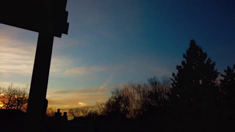 Wide-time-lapse-of-winter-sunset-from-the-balcony-of-a-house,-panning-left-to-right,-with-fast-moving-clouds-and-trees-moving-in-the-wind