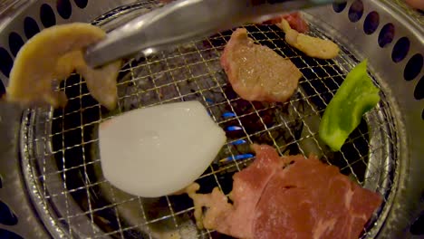 Two-Tongs-flipping-raw-meat-and-vegetables-on-yakiniku-Japanese-BBQ