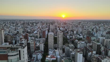 Aerial-track-right-of-Belgrano-neighborhood-buildings-and-skyscrapers-at-sunset-with-bright-sun-in-background,-Buenos-Aires,-Argentina