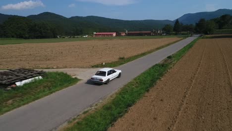 Aerial-tracking-shot-over-BMW-car-model-e30-driving-through-cultivated-fields