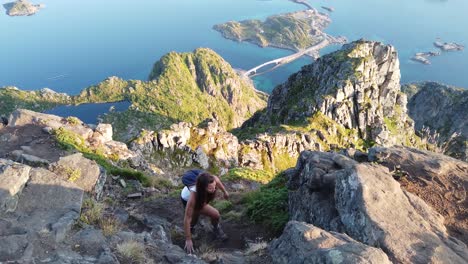 A-young,-fit-woman-is-climbing-up-the-cliff-of-Festvågtind-mountain-with-her-backpack-and-hiking-boots